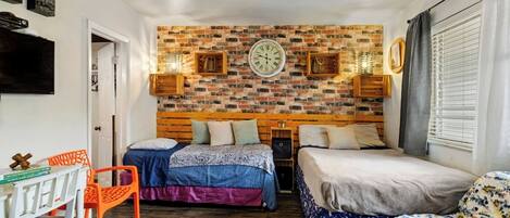 A compact room with a brick-patterned wall, a wooden bed, a small desk, and a chair.