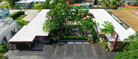 Vista aérea de um estacionamento com um edifício no centro, rodeado por árvores e uma pequena área de terraço.