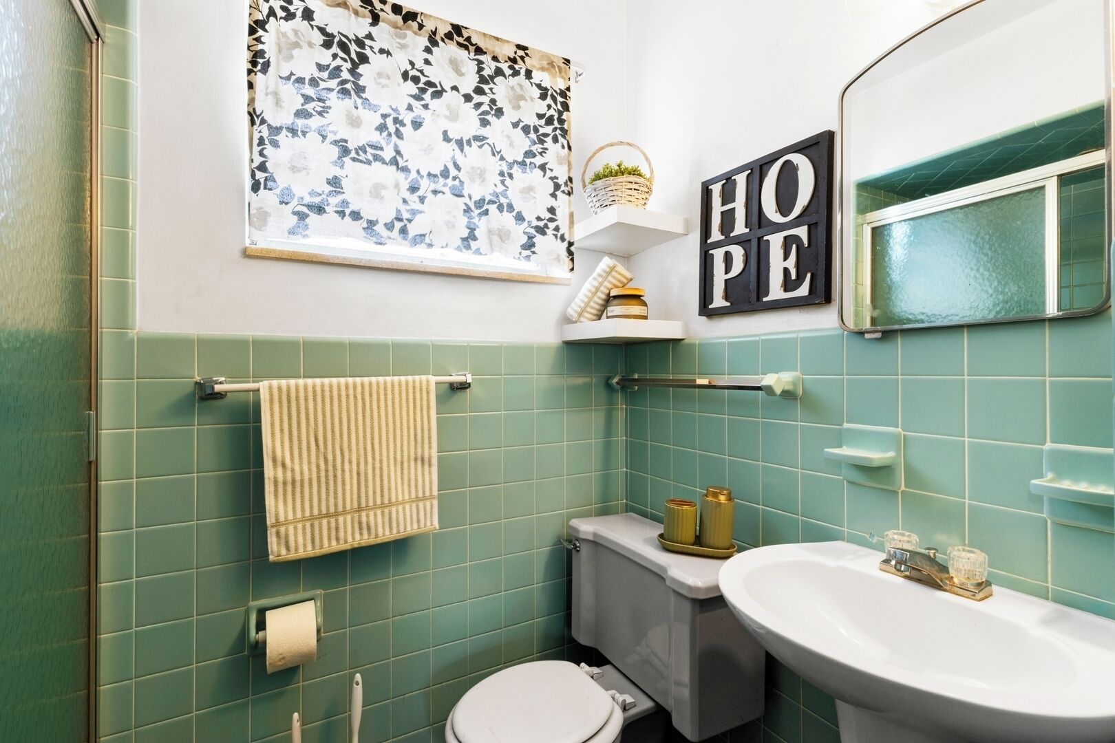 Une salle de bain avec des carreaux verts, des toilettes blanches, un lavabo, un porte-serviettes, un miroir et un panneau indiquant le mot « ESPOIR ».