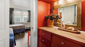 A room with a bed, a window with curtains, a mirror, and a wooden dresser with drawers.