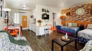 A compact living space with a kitchenette, a dining area, and a bedroom with a brick wall and a clock.