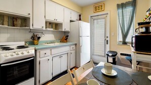 A compact kitchen with white cabinets, a stove, and a sink. There's a dining area with a table and chairs. - Pet Friendly Stylish Studio in Hollywood (Hollywood)