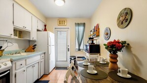 A compact kitchen with white cabinets, a stove, and a dining area with a wooden table and chairs. - Pet Friendly Stylish Studio in Hollywood (Hollywood)