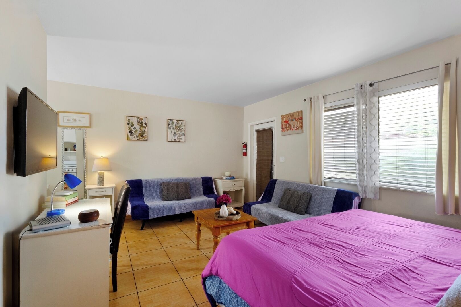 Ett rum med två soffor, en säng, ett skrivbord med en lampa och en tv.