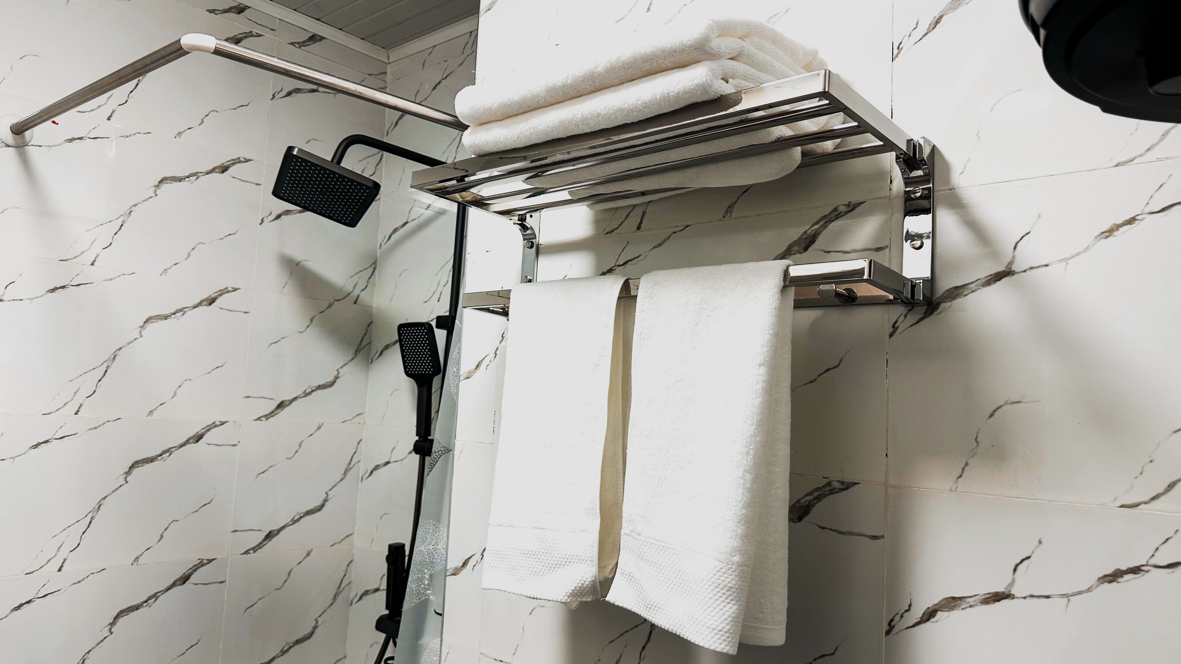 Un baño con ducha, toallero y toallas, y pared con estampado de mármol.