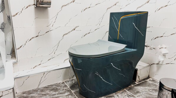 A modern bathroom with a marble wall and floor, a dark blue toilet, and a shower area. - Taj Mahal (Osh)