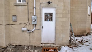 A beige brick building with a white door, electrical boxes, and a ladder leaning against the wall. - Cozy 3BR Near UB & Niagara Falls - Pet Friendly (Buffalo)