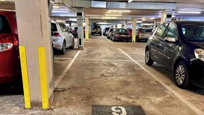 Un garaje para estacionamiento con varios coches aparcados en filas, suelo de hormigón y un espacio libre numerado.