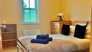 Un dormitorio con estructura metálica para la cama, una mesita de noche con lámpara, un aparador y una ventana con persianas.