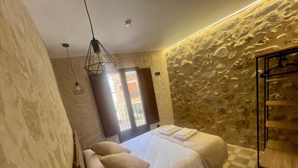 Une chambre avec un lit, un luminaire suspendu, un mur en pierre et un sol à carreaux.