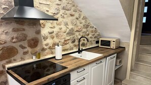 Une cuisine avec un mur en pierre derrière l’évier, une hotte noire, un four à micro-ondes, un évier et des armoires blanches.