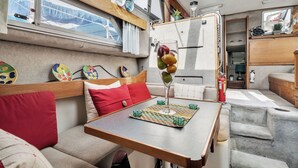 A cozy interior with a wooden table, cushioned seating, and a window overlooking a marina. - Luxury Yacht 2 BR Marina Views & Wifi (Anacortes)