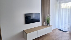 A modern living room with a flat-screen TV mounted on the wall, a wooden console table, and a potted plant. - Meerzeit apartment with terrace & parking space (Scharbeutz)