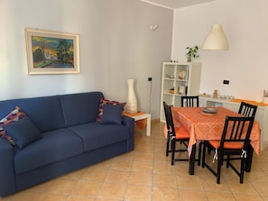 Un salon comprenant un canapé, une table à manger, des chaises, une bibliothèque et un tableau accroché au mur.