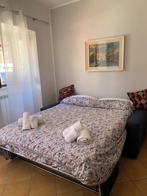 A hotel room with a bed, a painting on the wall, and a window with curtains.
