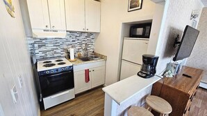 Une cuisine de taille réduite, dotée de meubles blancs, d’une cuisinière, d’un four à micro-ondes, d’un réfrigérateur et d’une machine à café.