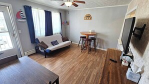Un salon comprenant un canapé, une table à manger, un ventilateur de plafond et un téléviseur fixé au mur.