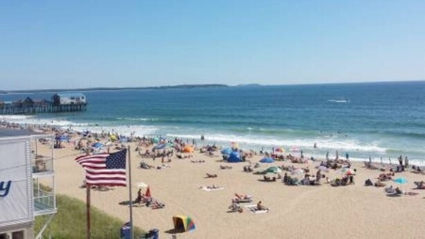 Une plage avec une jetée en arrière-plan, un drapeau et des personnes se détendant sur le sable.
