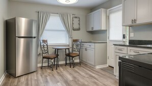 A modern kitchen with a stainless steel refrigerator, a dining table with two chairs, and white cabinetry. - Cozy 2BR Home: With Lake Access & Work Space (Mercer)