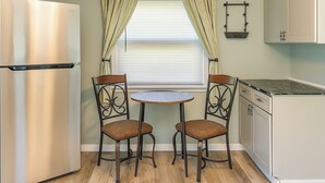 A compact kitchen with a stainless steel refrigerator, two chairs with woven seats, a small round table, and a window with blinds. - Cozy 2BR Home: With Lake Access & Work Space (Mercer)