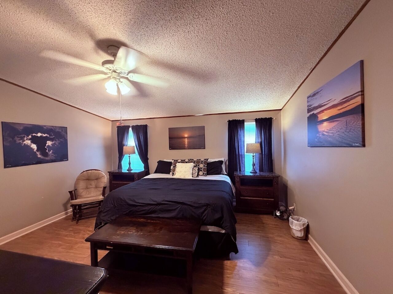 A bedroom with a bed, a chair, a desk, a ceiling fan, and artwork on the walls.