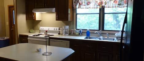 A kitchen with wooden cabinets, a stove, a sink, and a window with a floral curtain.