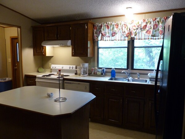 A kitchen with wooden cabinets, a stove, a sink, and a window with a floral curtain.