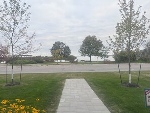 A paved pathway leading to a parking area with benches and trees. - Lakefront Living Downtown Orillia. (Orillia)