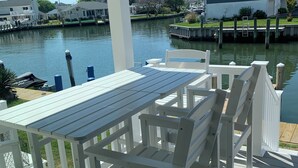 A covered outdoor deck with a table and chairs, overlooking a body of water and a residential area. - Charming 2-bedroom townhome with bay front views in delightful Ocean City (Ocean City)