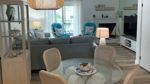 A modern living room with a glass dining table, wicker chairs, a grey sofa, and a large window. - Charming 2-bedroom townhome with bay front views in delightful Ocean City (Ocean City)