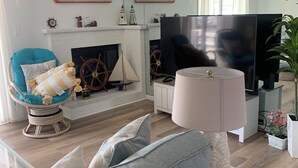 A living room with a fireplace, a large flat-screen TV, a teal armchair, and a grey sofa. - Charming 2-bedroom townhome with bay front views in delightful Ocean City (Ocean City)