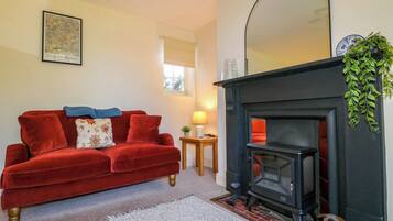 Una sala de estar acogedora con un sofá de terciopelo rojo, una chimenea, un espejo y un cuadro en la pared.