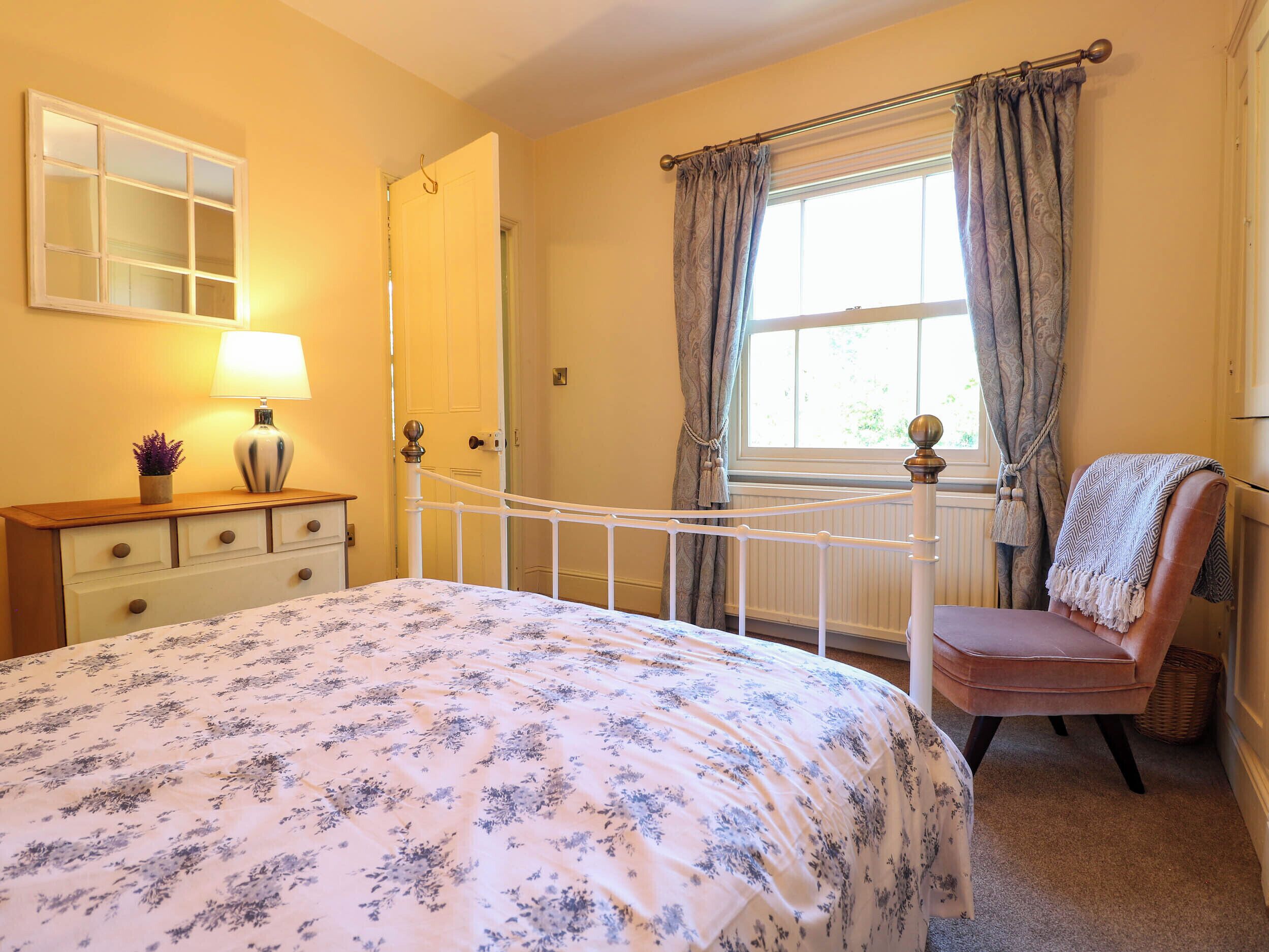 A bedroom with a bed, a dresser, a chair, a window with curtains, and a lamp on a nightstand.