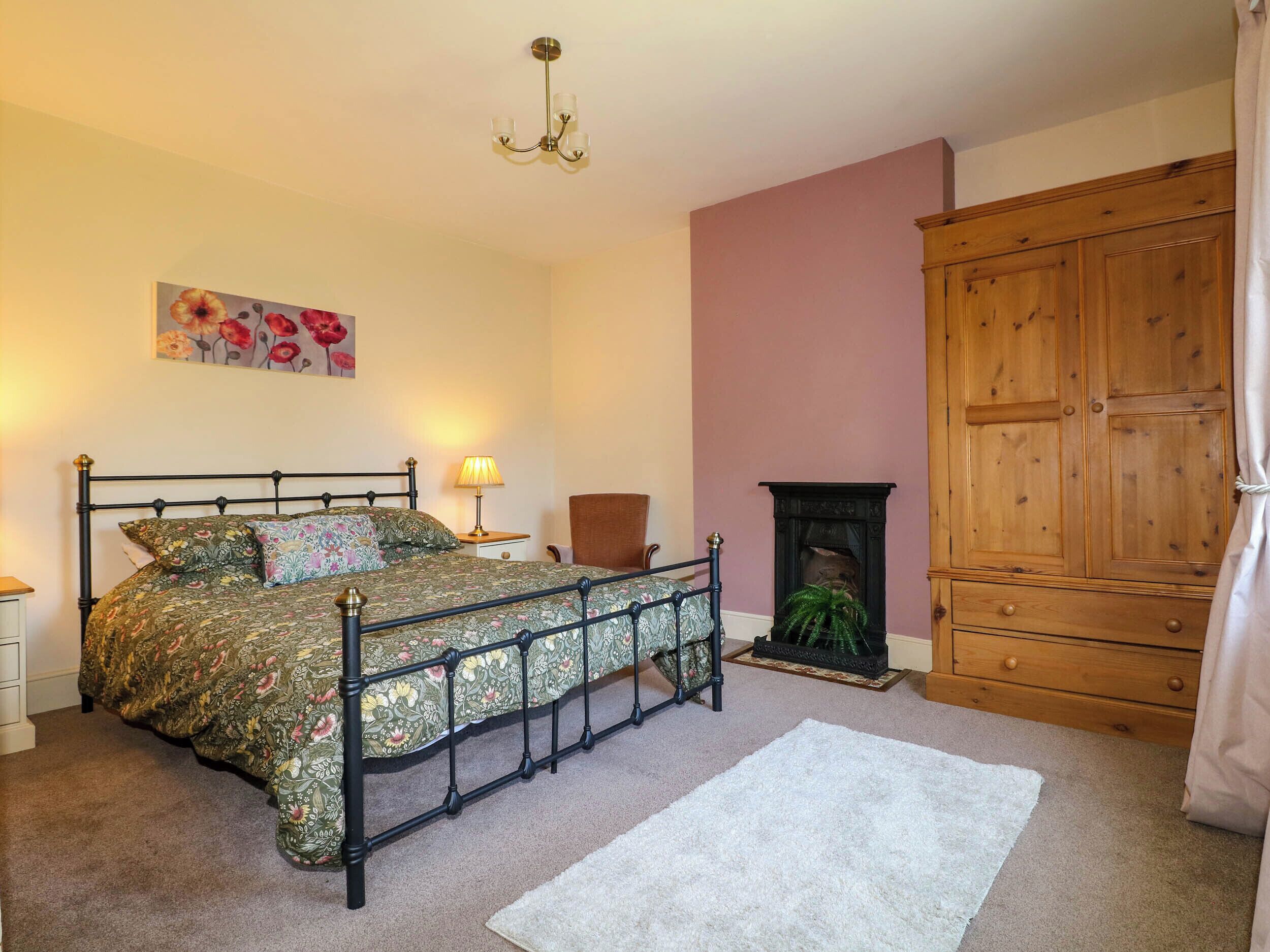 A bedroom with a four-poster bed, a wooden wardrobe, a fireplace, and a painting on the wall.