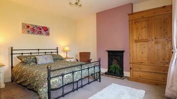 A bedroom with a four-poster bed, a wooden wardrobe, a fireplace, and a painting on the wall.