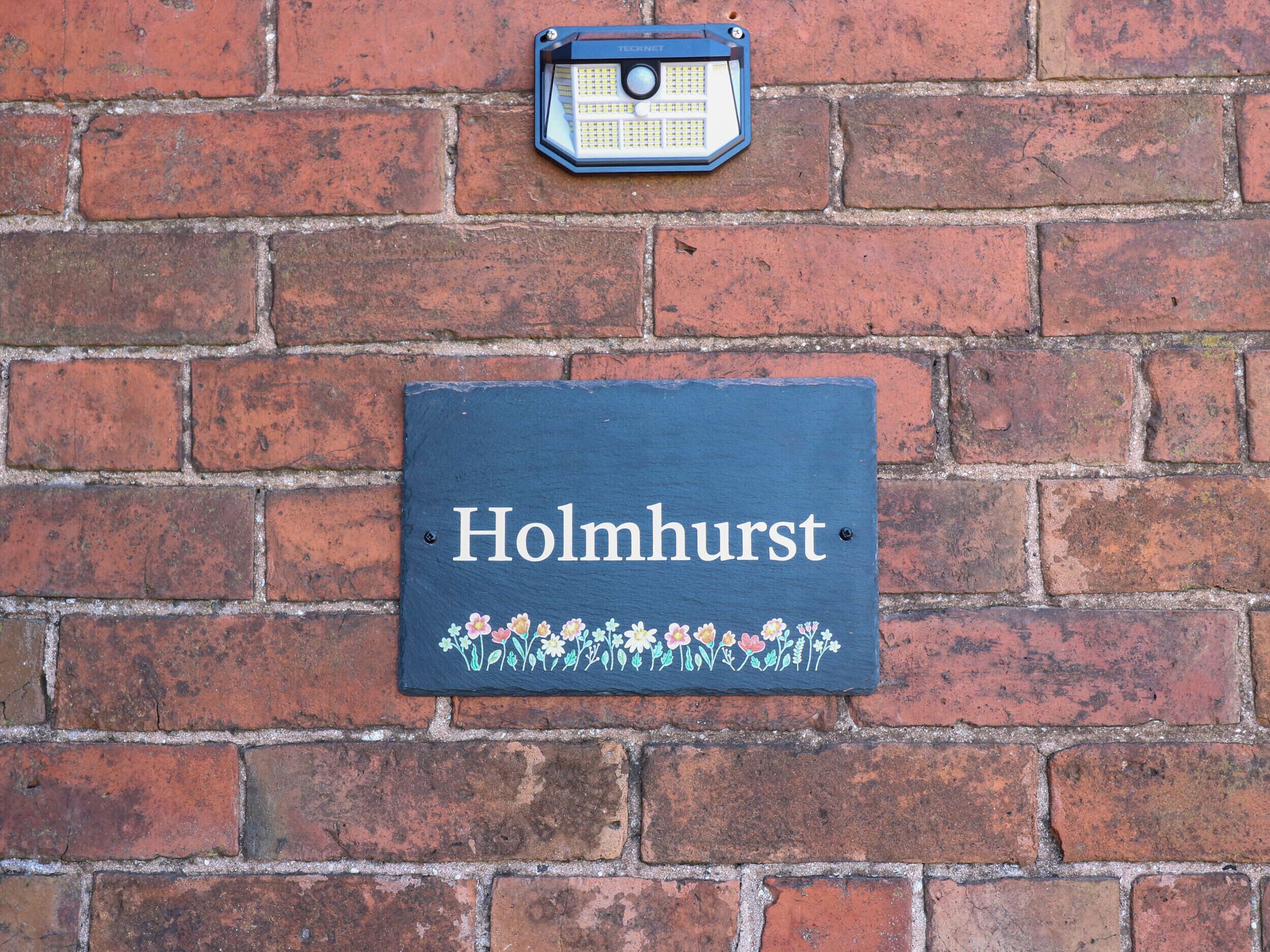 A brick wall with a sign reading "Holmhurst" and a weather station mounted above it.