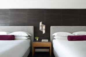 Habitación de hotel con dos camas, una mesita de noche de madera, un adorno en la pared y una planta pequeña.