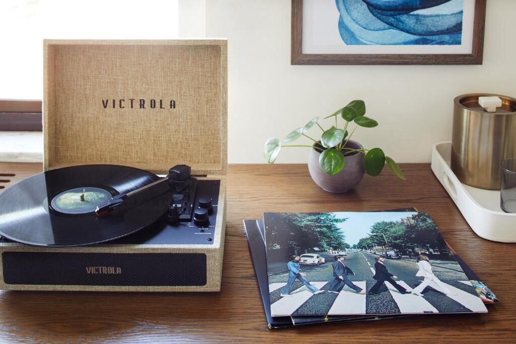 A turntable with a vinyl record, a vinyl record box, a framed picture, a potted plant, and a candle holder on a wooden table.