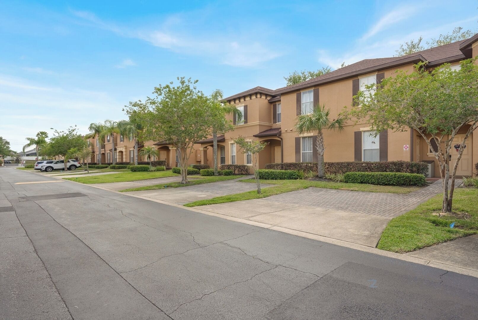 A row of townhouses with a paved driveway and small trees in front.