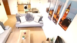 A living room with a sofa, a coffee table, and a small plant. There are framed pictures on the wall.