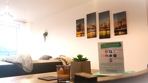 A hotel room with a bed, a bedside table with a glass of water, a plant, and a poster on the wall.