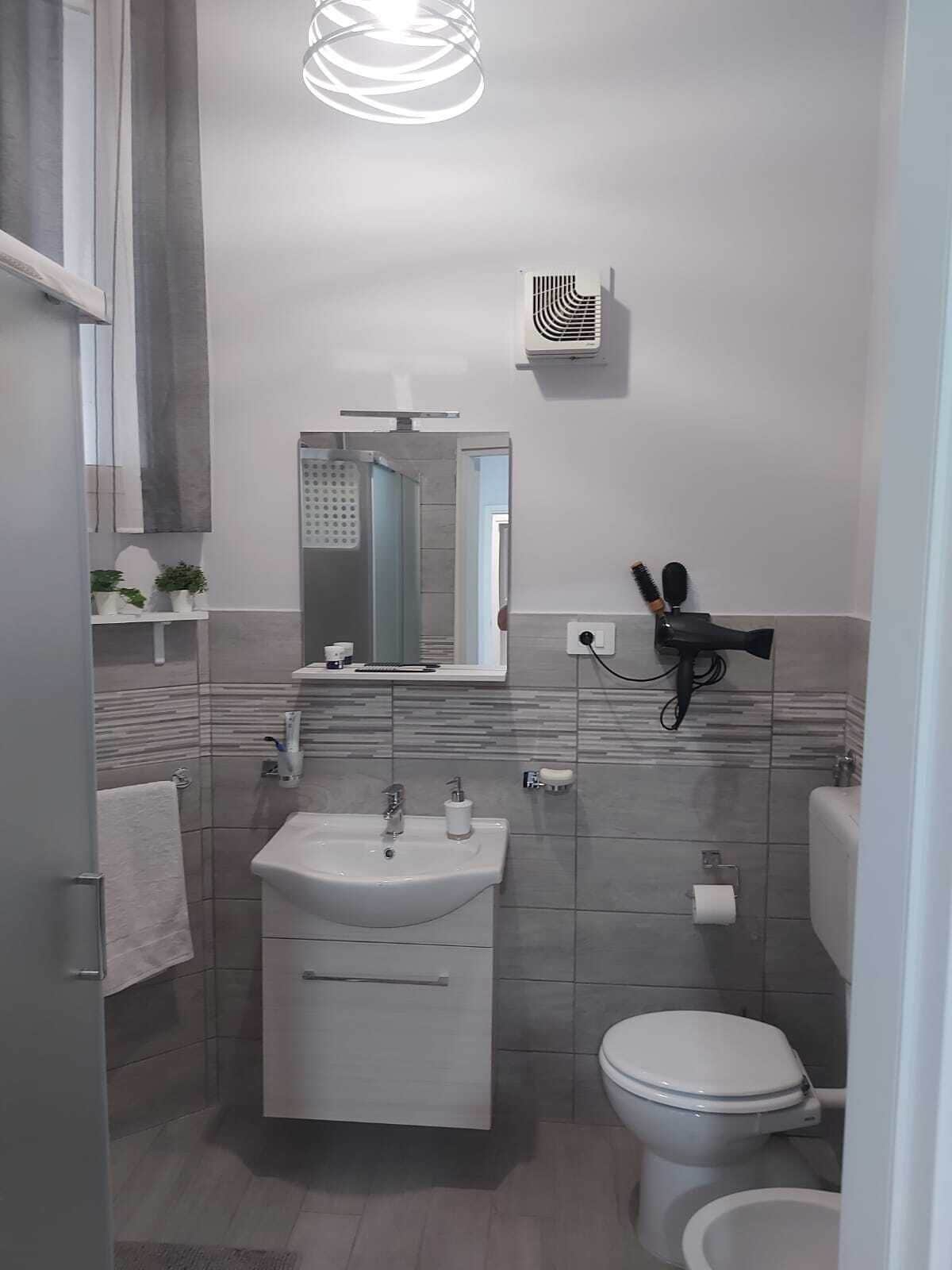 A modern bathroom with a glass-enclosed shower, a white sink, a toilet, and a hairdryer mounted on the wall.