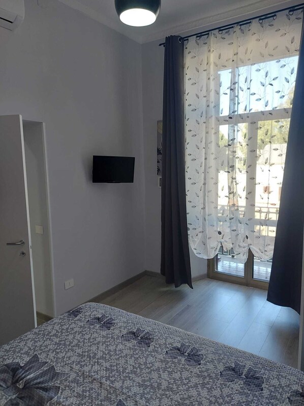 A bedroom with a bed, a TV mounted on the wall, a door, and a window with curtains. - Alloggio Turistico Sea Port - Next to the Cruise Ship Free Shuttle Terminal (Civitavecchia)