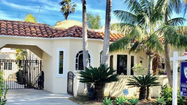 A residential property with a tiled roof, a gated entrance, and a well-maintained garden with palm trees and shrubs.