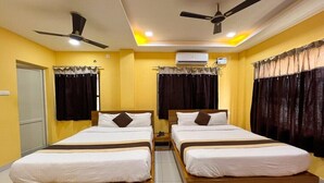 A hotel room with two single beds, ceiling fans, an air conditioning unit, and curtains. - Cholas Castle inn (Tiruchirappalli)