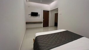 A modern hotel room with a large bed, a flat-screen TV mounted on the wall, and a small desk area. - Cholas Castle inn (Tiruchirappalli)