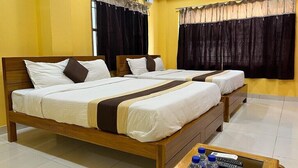 A hotel room with two wooden beds, a small table with water bottles and a remote control, and an air conditioning unit on the wall. - Cholas Castle inn (Tiruchirappalli)