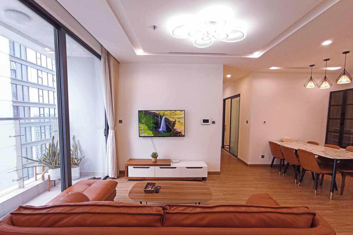 Ein modernes Wohnzimmer mit großem Fenster, einer Couch, einem Couchtisch und einem an der Wand befestigten Fernseher.