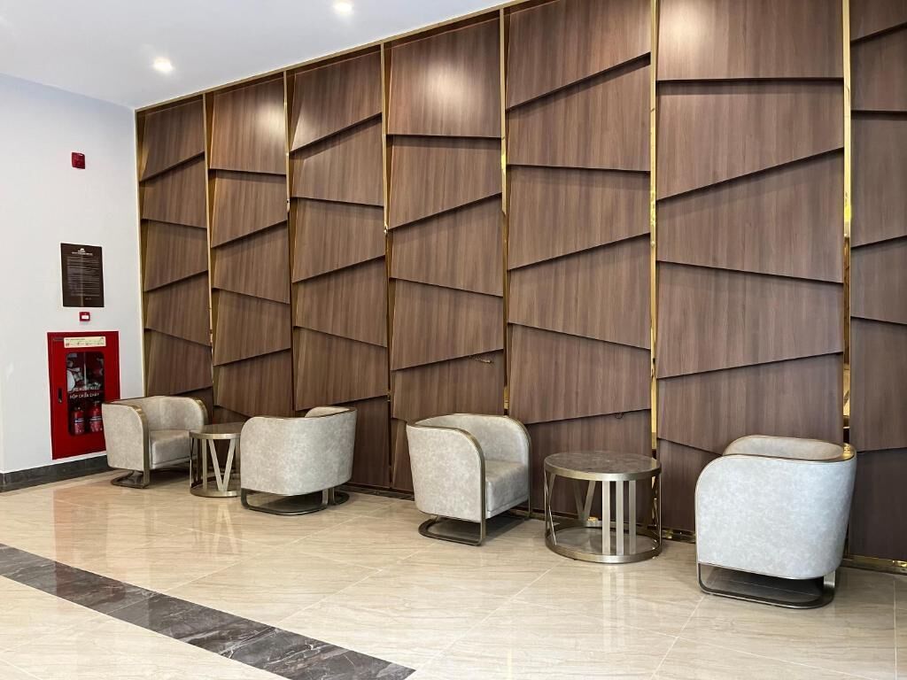 A lobby with a modern design, featuring a wall with geometric patterns and a row of seating areas with chairs and a small table.