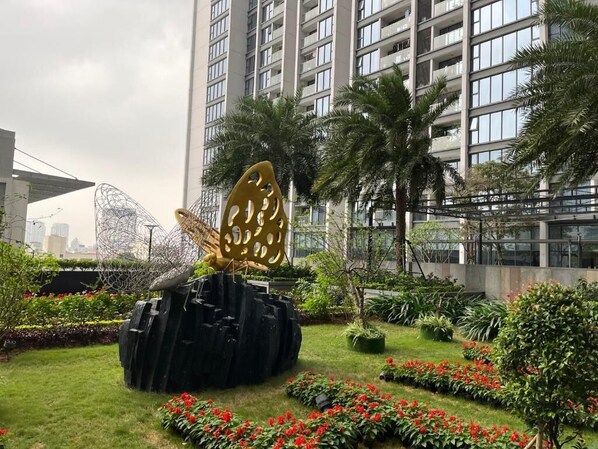 A landscaped garden with a large golden sculpture, palm trees, and red flowers.